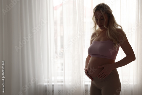 Free Download Beautiful pregnant woman near window at home. Space for text - GFXLoad