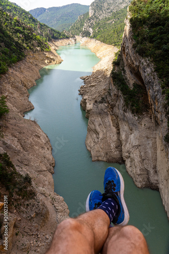 Person sitting on cliff edge overlooking turquoise canyon river reservoir