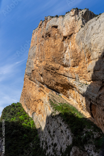 Massive limestone cliff face with golden sunlight in mountain gorge