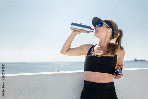 Fitness enthusiast enjoys a refreshing drink while taking a break by the waterfront on a sunny day