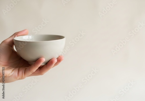 Human Hand Holding an Empty White Ceramic Bowl Against Neutral Background