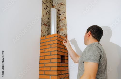 A young man makes brickwork on the chimney of a fireplace.