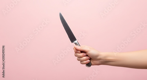 Woman's Hand Holding a Stainless Steel Kitchen Knife on Pink Background