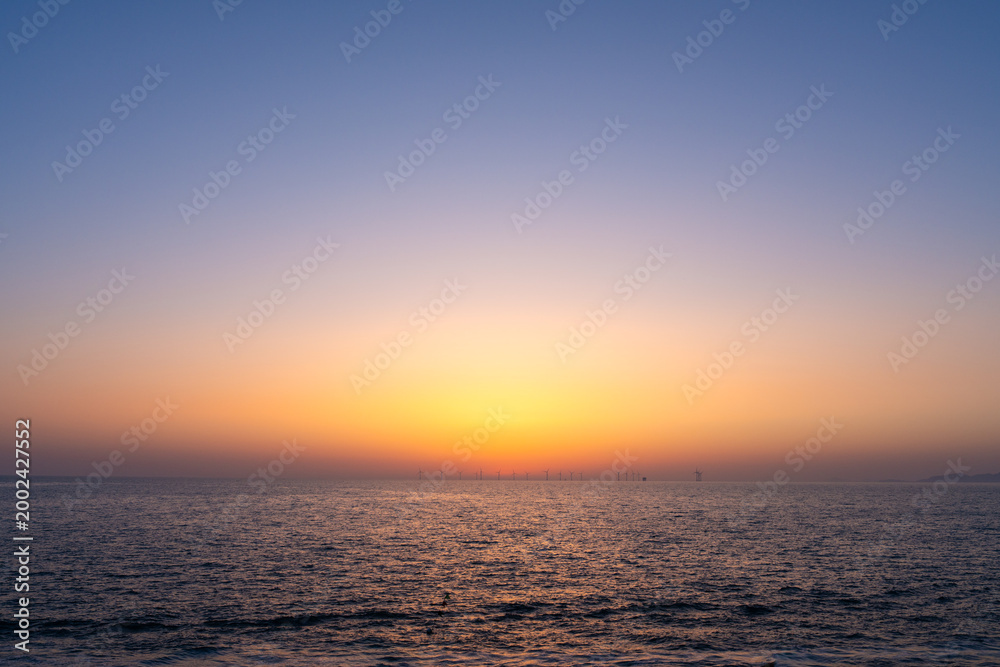 Obraz premium Minimalist Seascape with Golden Sunset Gradient and Distant Wind Farm