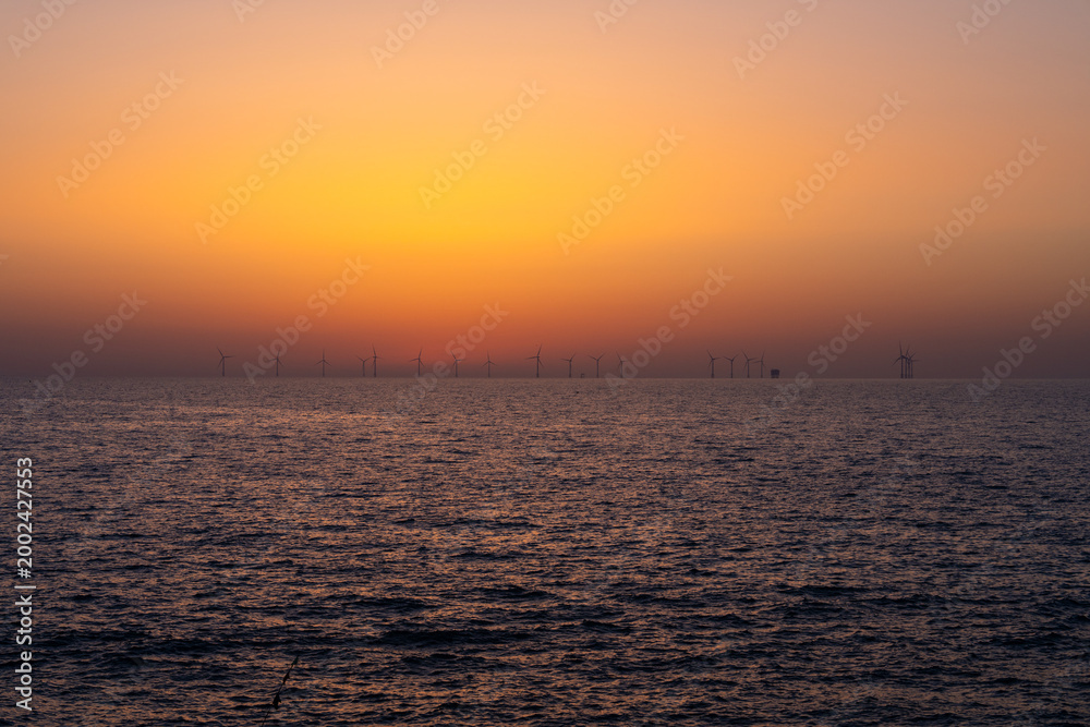 Obraz premium Offshore Wind Farm Silhouettes Against Golden Twilight Sky