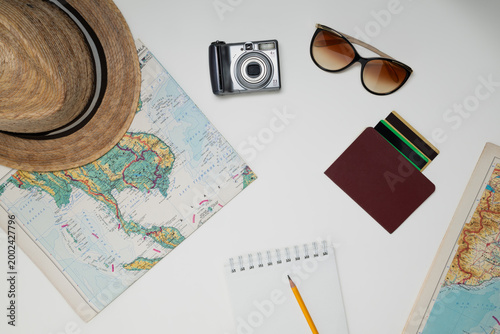 Obraz na plátně Flat lay of travel planning essentials including map, camera, sunglasses, hat, wallet and notebook on a clean white background with copy space