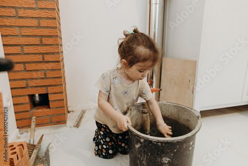 A little girl mixes cement mortar in a bucket.