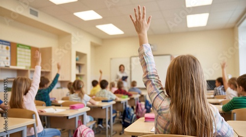 Elementary school children raise their hands in a brightly lit classroom while participating in an engaging educational activity with their teacher.