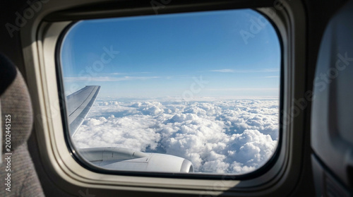 Airplane window view showing wing and engine above fluffy clouds under clear blue sky with soft natural light creating peaceful and serene atmosphere