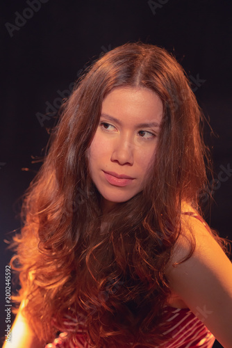 The young woman in a striped outfit displays a thoughtful pose and intriguing expression, highlighting her personality and depth against a contrasting dark background.