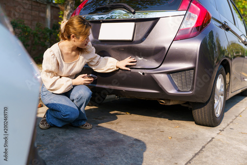 Woman inspecting damaged car bumper after minor accident
