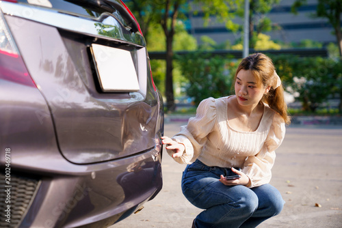 Fotografie Woman inspecting damaged car bumper after minor accident