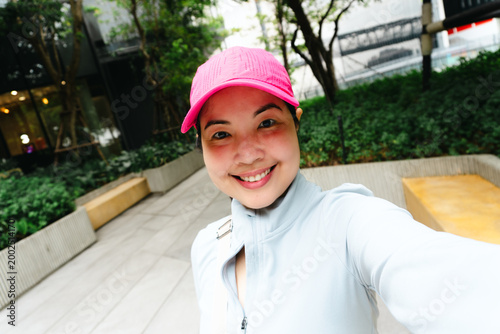 Cheerful Asian Woman in Pink Cap and Fitness Wear Taking a Selfie in an Urban Park