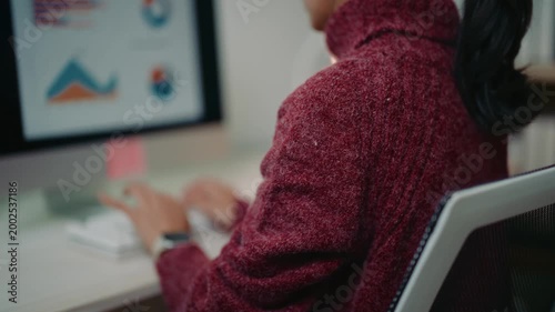 Professional woman typing on a keyboard, working on business charts and graphs on her desktop computer monitor in a modern home office