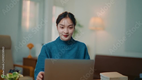 Cheerful asian student starting her day, opening her laptop and beginning to type. A young professional remote working from her apartment