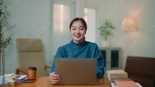 Happy young asian woman opening her laptop to start a new day of work. Cheerful female professional starting her workday with a smile