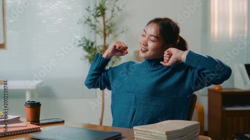 Happy Asian businesswoman closing her laptop, stretching her arms and relaxing on her chair after finishing a project at the office