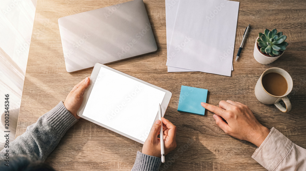 Obraz premium High-angle photograph of hands working efficiently on a modern digital tablet with a blank screen and stylus.
