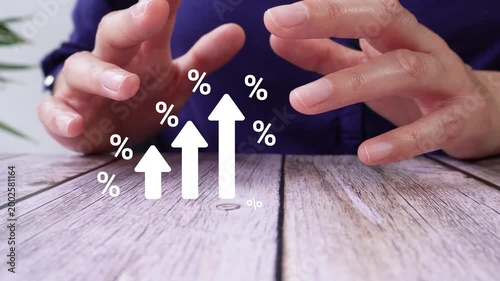 Close-up of a pair of hands on a table, shielding an animated graphic of white arrows rising, surrounded by percentage symbols. Ideal for charts, reports, or financial visual representations.