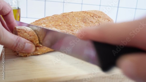 Hands cutting bread on a wooden board. The cutting motion suggests homemade baking or food preparation.
