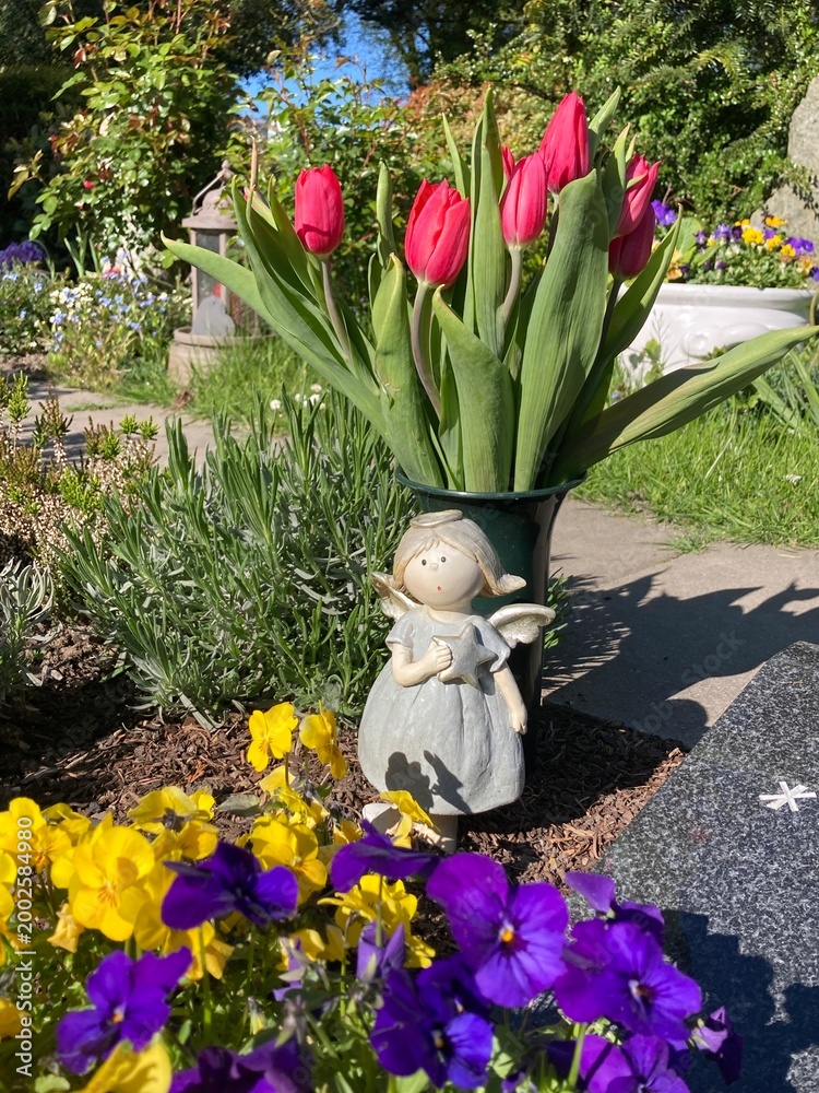 Obraz premium Tulpen, Blumen und Engel schmücken ein Grab auf dem Friedhof im Frühling 