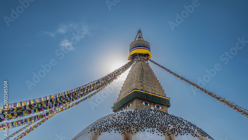 A huge stupa. The eyes of the Buddha are painted on the top. A spire against a clear blue sky. Rows of bright multicolored flags. A flock of pigeons on the dome. Nepal. Kathmandu. Boudhanath Stupa