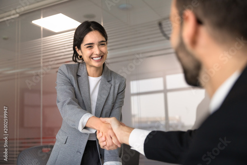 Portrait of happy female applicant and HR manager shaking hands in meeting room, finalizing job interview representing successful hiring, employment and professional partnership in company office