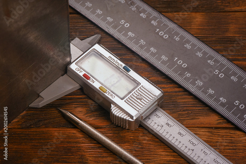 Obraz na płótnie Digital caliper measuring metal sheet with steel ruler and metal scribe on wooden workbench table close up background
