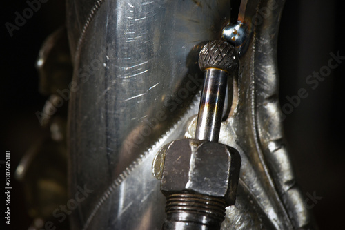 Electric straight grinder with carbide burr grinding steel surface on dark workshop close up background.