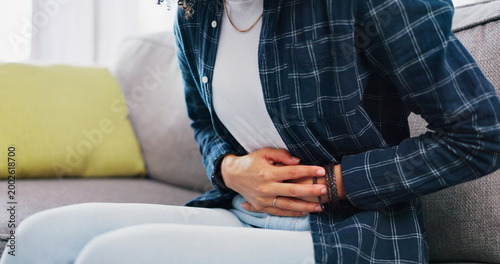 Foto Woman, hands and sofa with stomach ache in home for menstruation, pain or period cramps