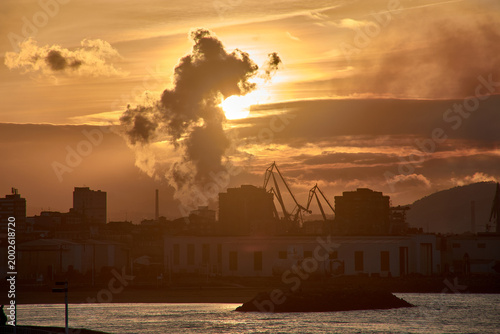 A gijon sunset obscured by industrial smoke, casting a dramatic silhouette