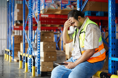 Worker feeling exhausted and overwhelmed, leaning on a storage rack in a warehouse