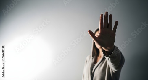 Woman with her hand outstretched in a stopping motion against a gray background with a bright light source