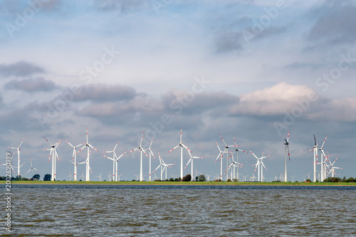 Modern wind turbines for renewable energy at Neufelderkoog, on green dike near the mouth of Elbe river, Schleswig-Holstein, Northern Germany