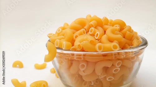 Elbow Macaroni Pasta Dropping in Glass Bowl on White Background, Uncooked Elbow Macaroni Pasta Ingredient