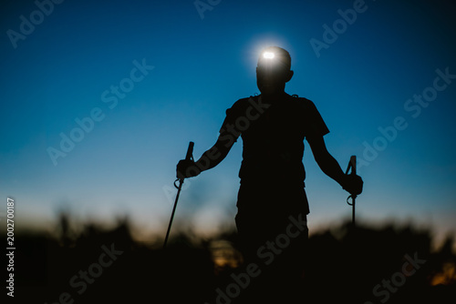 Silhouette of a Male Trail Runner with Headlamp and Trekking Poles at Dusk