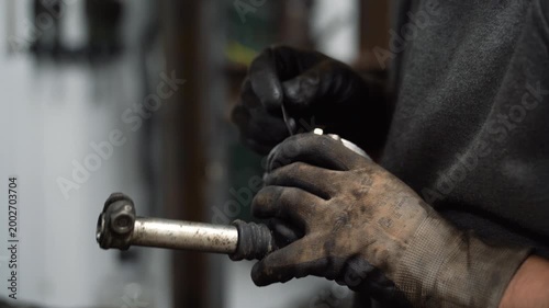 A mechanic cleans car parts by cutting off excess glue from a gearshift lever.