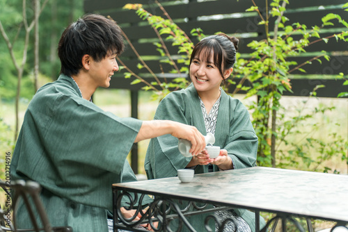 Принти на полотні A couple in yukata (traditional Japanese summer kimonos) pouring sake for each other on the garden terrace of a ryokan (traditional Japanese inn)