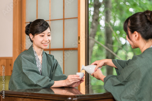 Cuadro en lienzo A woman and her friend drinking sake on the veranda of a Japanese-style room in a traditional Japanese inn, both wearing yukata robes