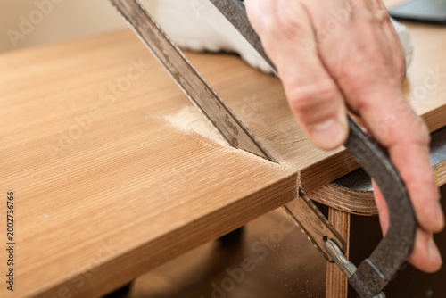Closeup photo of carpenter hand with saw cutting wooden board Cutting plywood board with hand saw during home renovation work