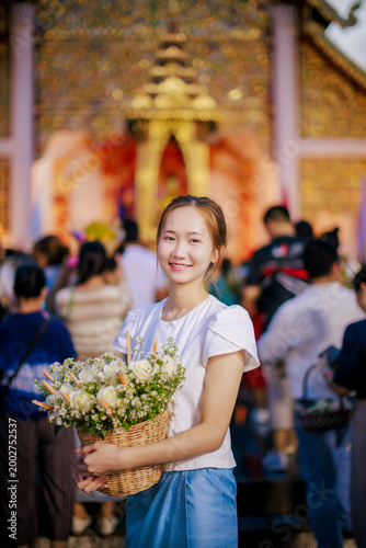Beautiful Asian woman in Lanna dress holding flower basket for Inthakin City Pillar Festival or Sai Khan Dok tradition at Wat Chedi Luang Temple at evening, Chiang Mai, Thailand 