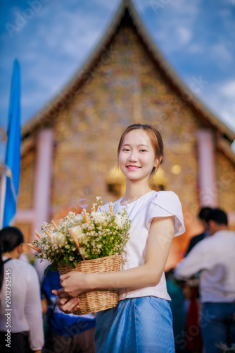 Beautiful Asian woman in Lanna dress holding flower basket for Inthakin City Pillar Festival or Sai Khan Dok tradition at Wat Chedi Luang Temple at evening, Chiang Mai, Thailand 