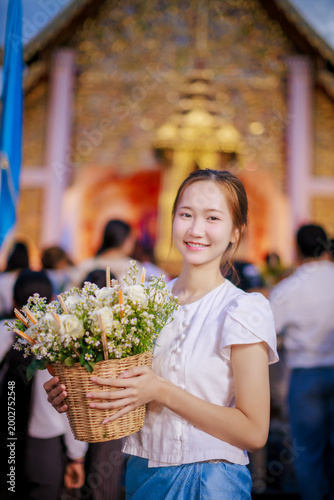 Beautiful Asian woman in Lanna dress holding flower basket for Inthakin City Pillar Festival or Sai Khan Dok tradition at Wat Chedi Luang Temple at evening, Chiang Mai, Thailand 