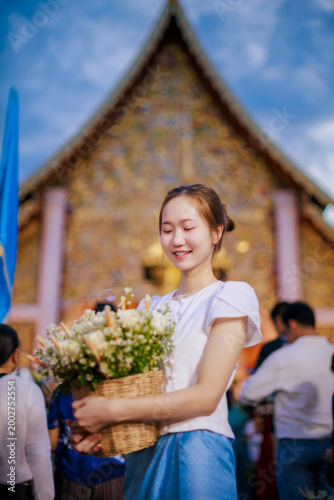 Beautiful Asian woman in Lanna dress holding flower basket for Inthakin City Pillar Festival or Sai Khan Dok tradition at Wat Chedi Luang Temple at evening, Chiang Mai, Thailand 