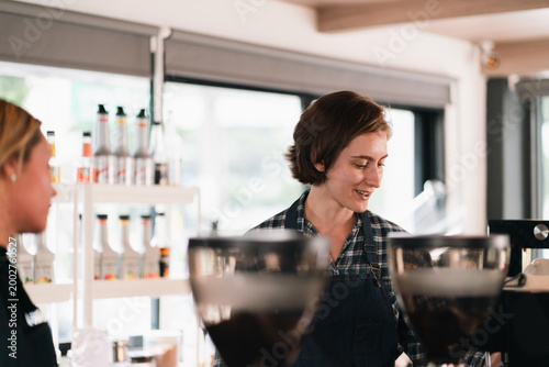 Barista working in coffee shop with smiling colleague and blurred coffee equipment in foreground