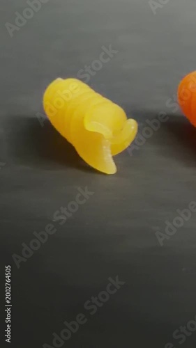 Colorful uncooked snail shaped fusilli pasta rotating slowly on a dark, textured background, revealing intricate details of the semolina and vegetable powder ingredients