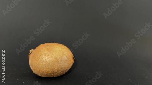 Woman's hand carefully placing a fresh, ripe, organic whole kiwi fruit on a smooth dark background for a healthy lifestyle, diet, and nutrition concept