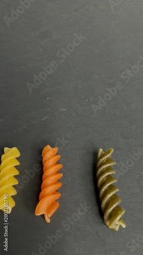 Colorful uncooked tricolor fusilli pasta with tomato and spinach flavor spinning and dancing on a dark stone background, showcasing a healthy and vibrant meal ingredient