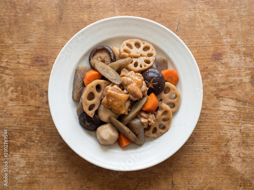 Delicious Chikuzenni featuring tender chicken, lotus root, shiitake mushrooms, and carrots simmered in a savory dashi soy sauce on a rustic wooden background.