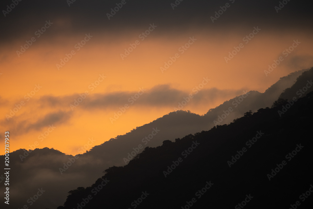 Fototapeta premium Layered Mountain Silhouettes at Sunset with Orange Sky